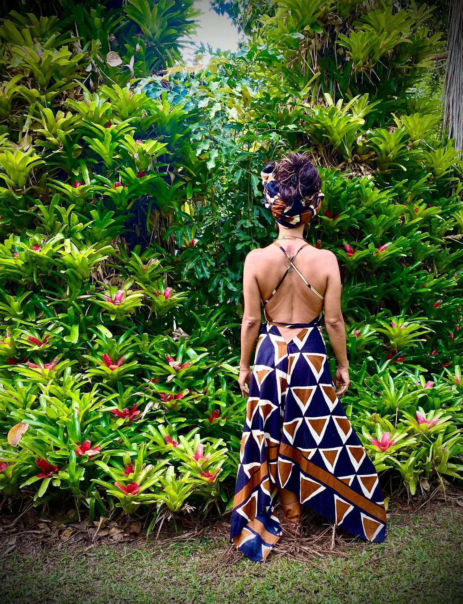 A woman wearing a stylish backless dress with geometric patterns, surrounded by lush greenery in a tropical setting, showcasing Ladies Dresses.