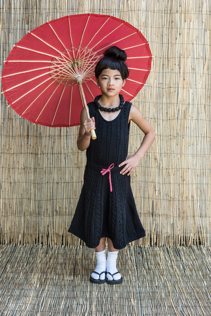 A girl wearing a Black Cable Knit Dress for Girls, holding a red parasol, with a stylish hairstyle and accessories.