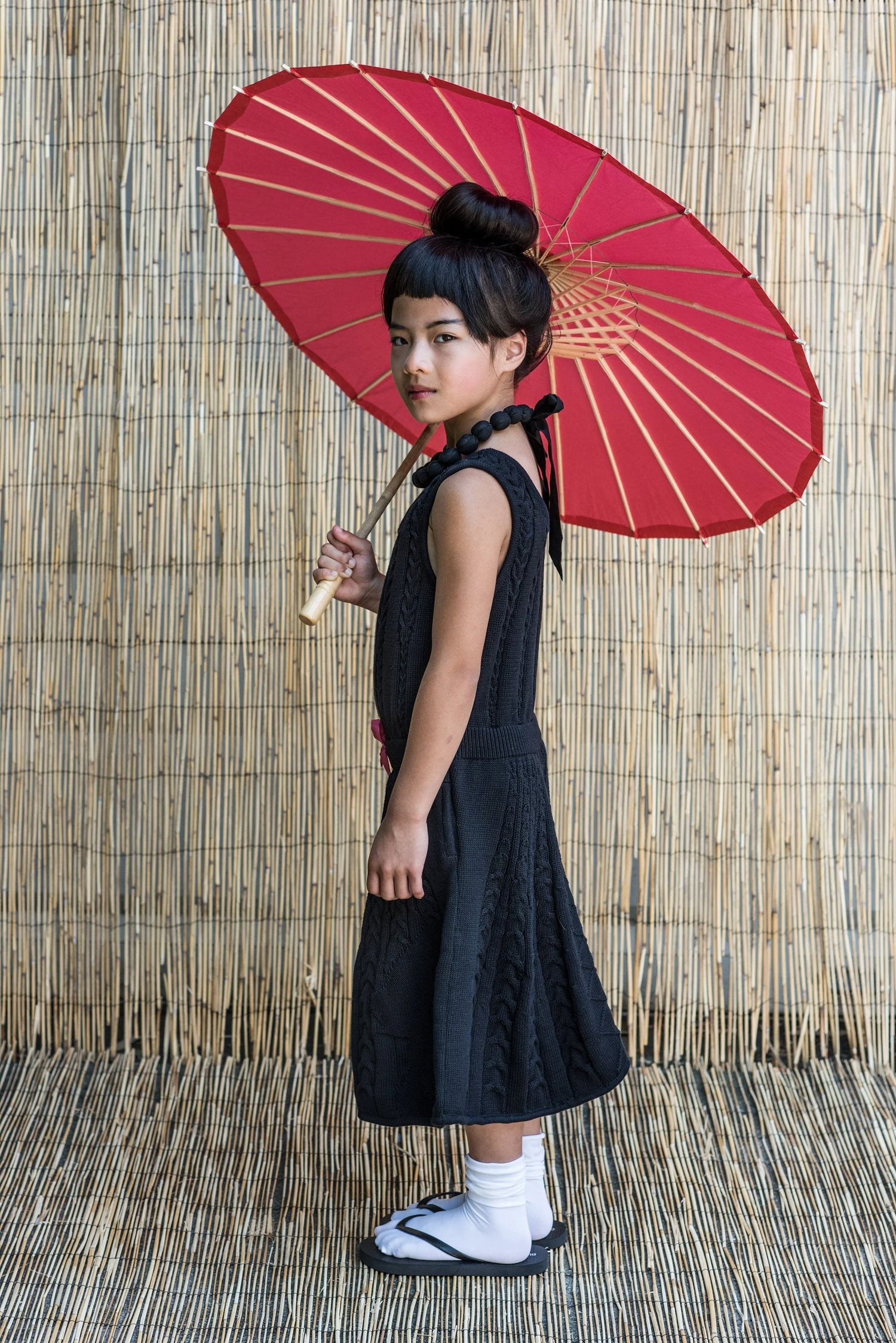 Black Cable Knit Dress for Girls worn by a girl holding a red parasol, showcasing elegance and style.