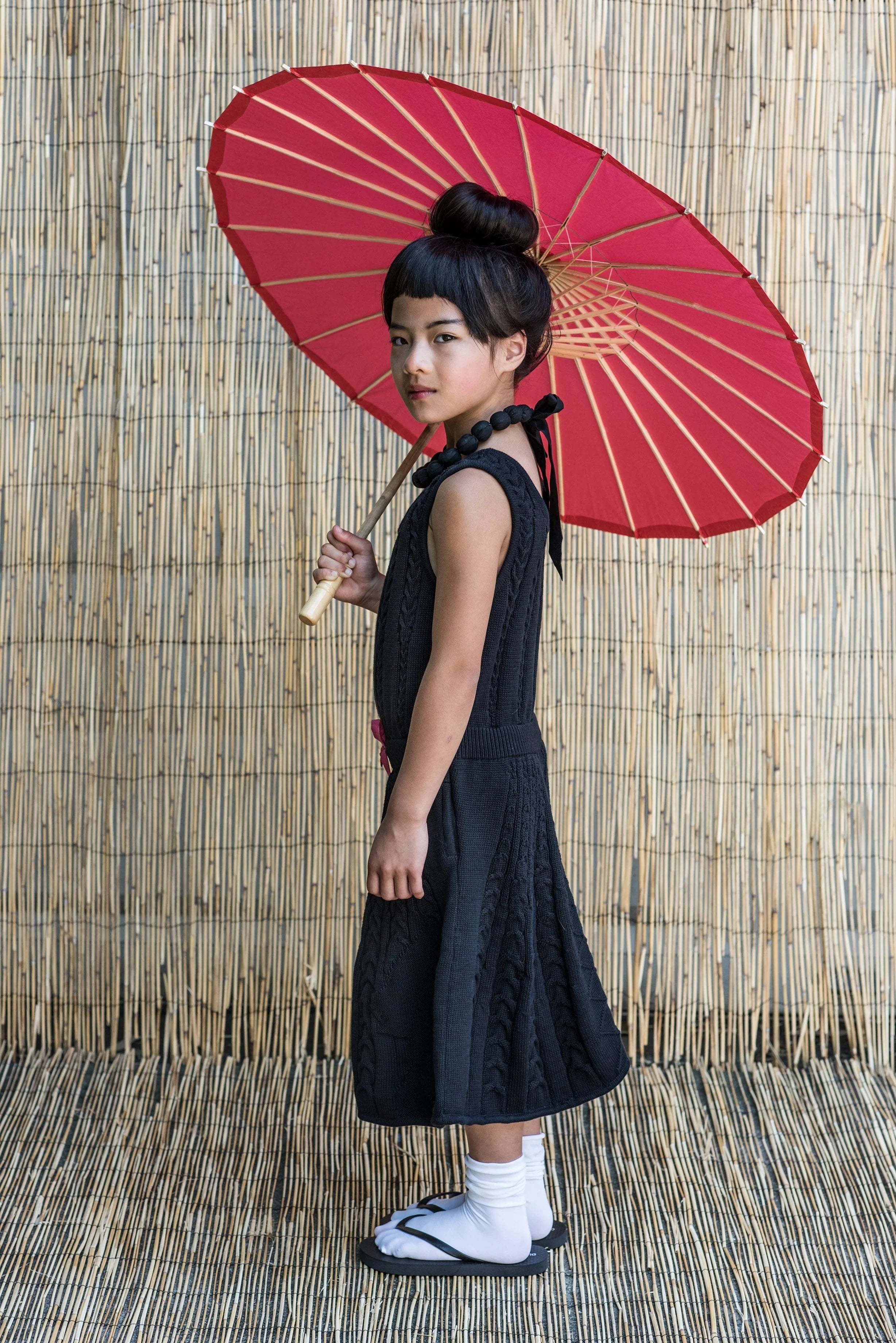 Black Cable Knit Dress for Girls worn by a girl holding a red parasol, showcasing elegance and style.