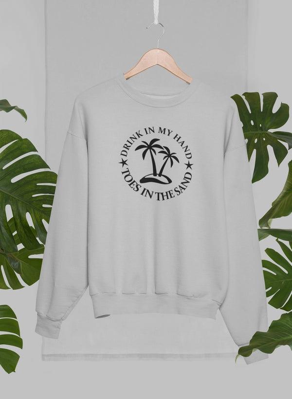 Drink In My Hand Toes In The Sand Sweat Shirt displayed on a hanger with tropical leaves in the background.