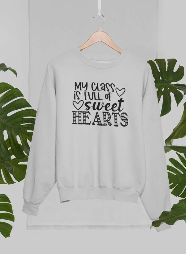 My Class Is Full Of Sweet Hearts Sweat Shirt displayed on a hanger among tropical leaves.