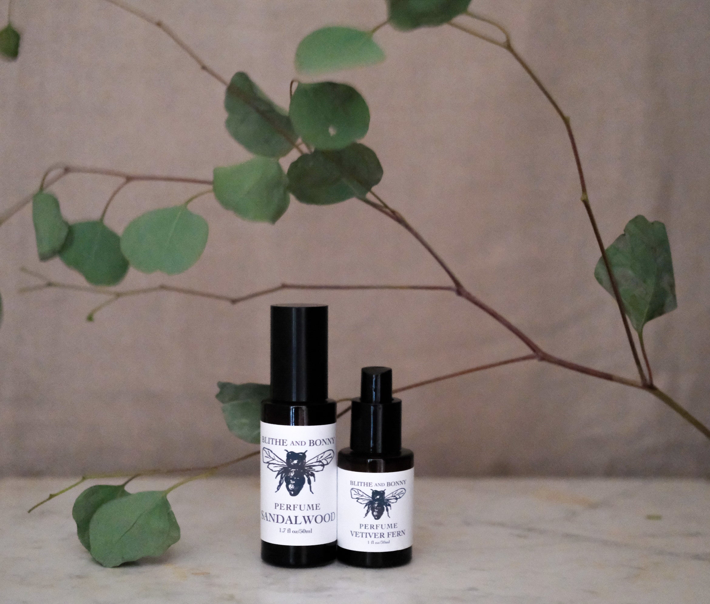 Petite Perfume in amber bottles with sandalwood scent surrounded by eucalyptus leaves.